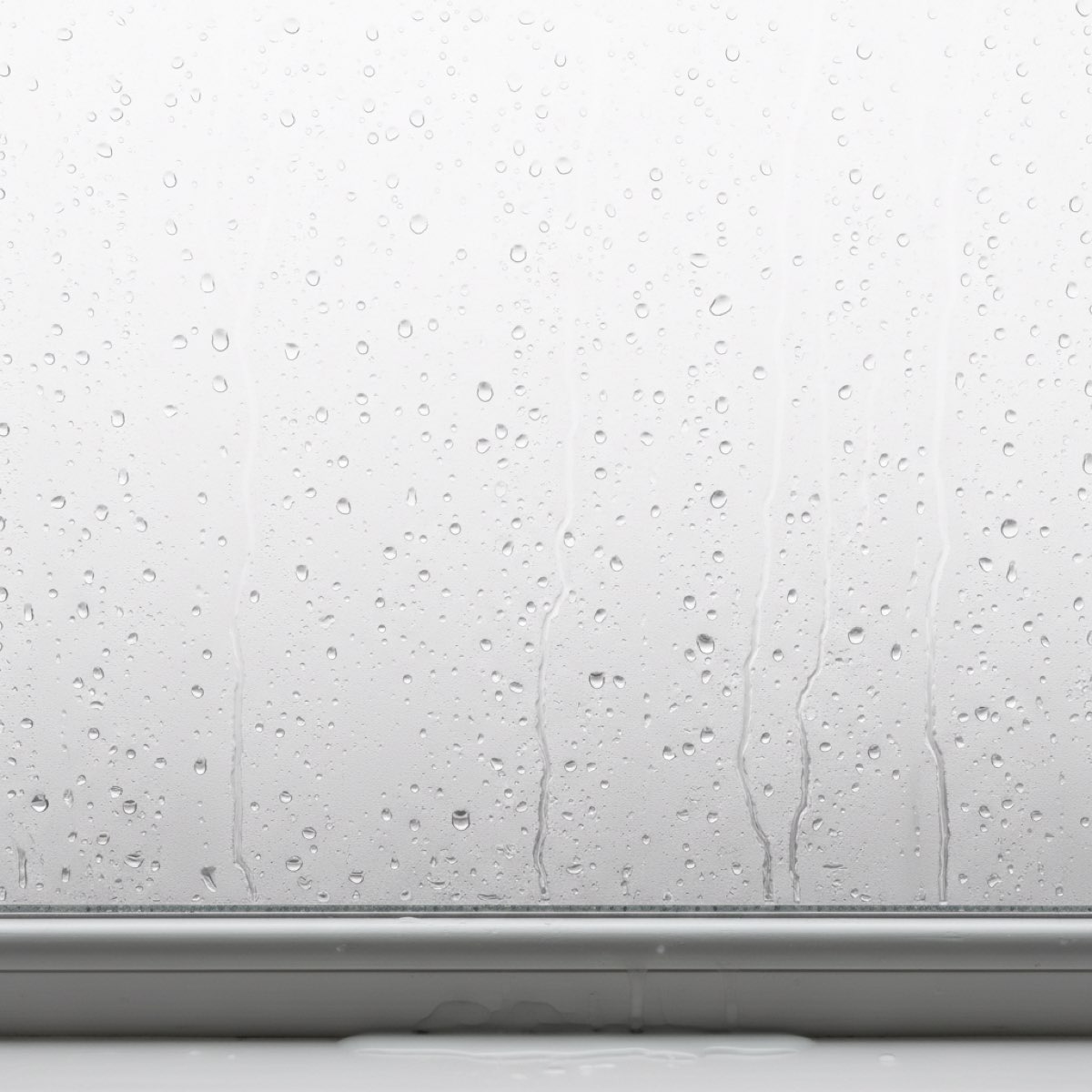 Heavy condensation beaded on the inside of a window pane, with rivulets running down the glass and water pooling on the sill